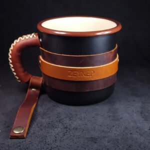 Black enamel mug wrapped in full-grain leather with a tan strap engraved ZEYNEP, laced leather handle