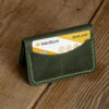 Personalized Compact Full-Grain Leather Card Holder — Neptün, Green Green full-grain leather compact card holder standing on a wooden table with a bank card in the front pocket