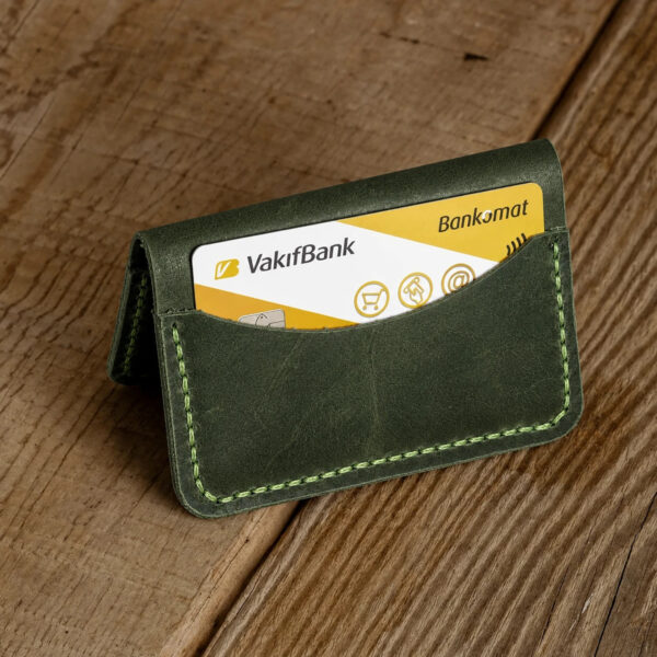 Personalized Compact Full-Grain Leather Card Holder — Neptün, Green Green full-grain leather compact card holder standing on a wooden table with a bank card in the front pocket