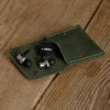 Green full-grain leather snap pouch opened on a wooden table with wired earphones inside