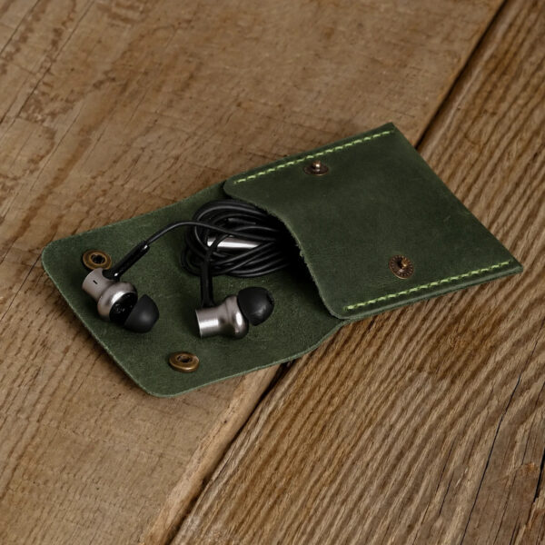 Green full-grain leather snap pouch opened on a wooden table with wired earphones inside
