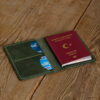 Personalized Full-Grain Leather Passport Holder — Alesta, Green Green full-grain leather passport holder opened on a wooden table with a passport and two cards inside